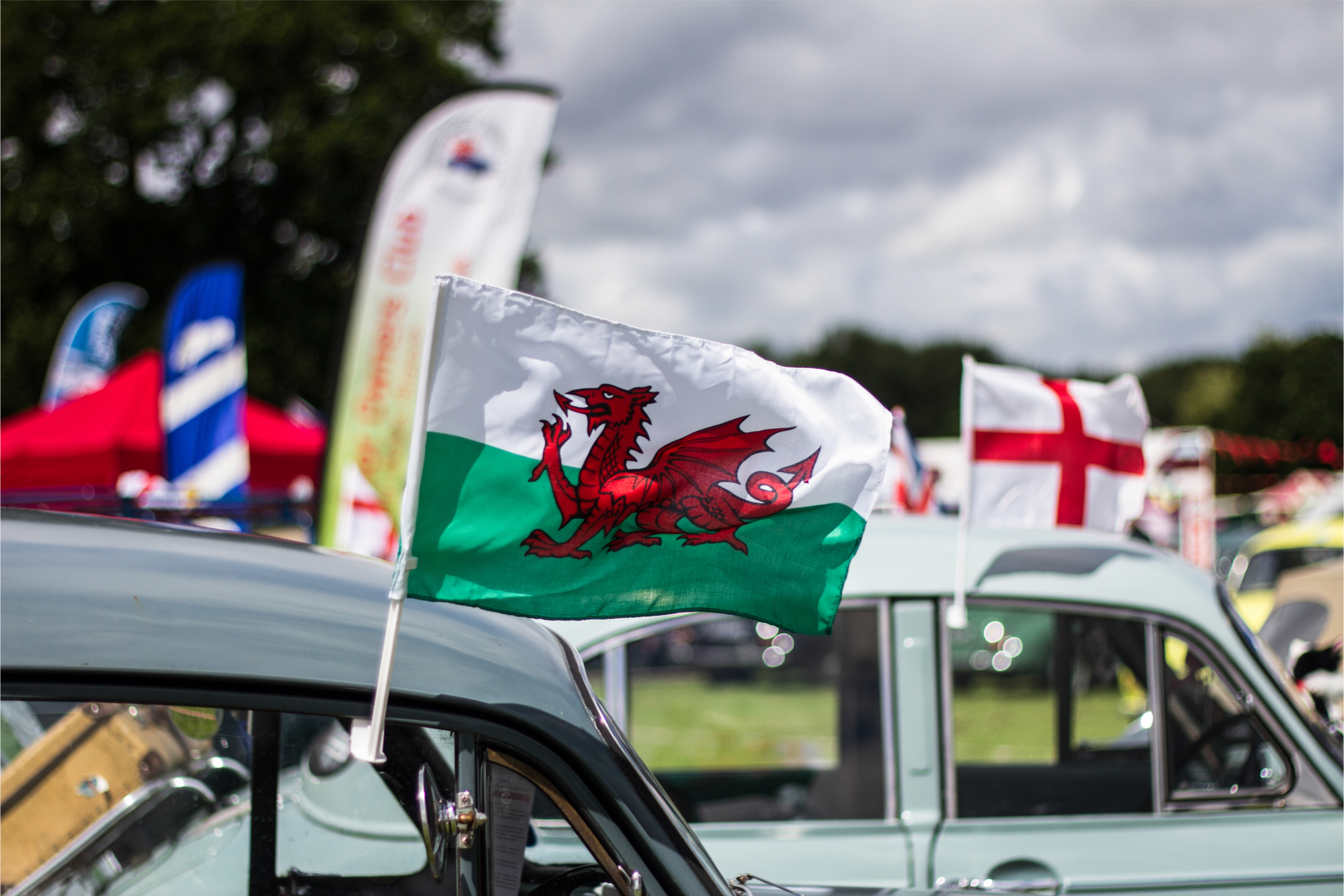 Welsh Flag displayed above the top of a Classic car with another car and St Georges Cross in background at a Classic Car Show