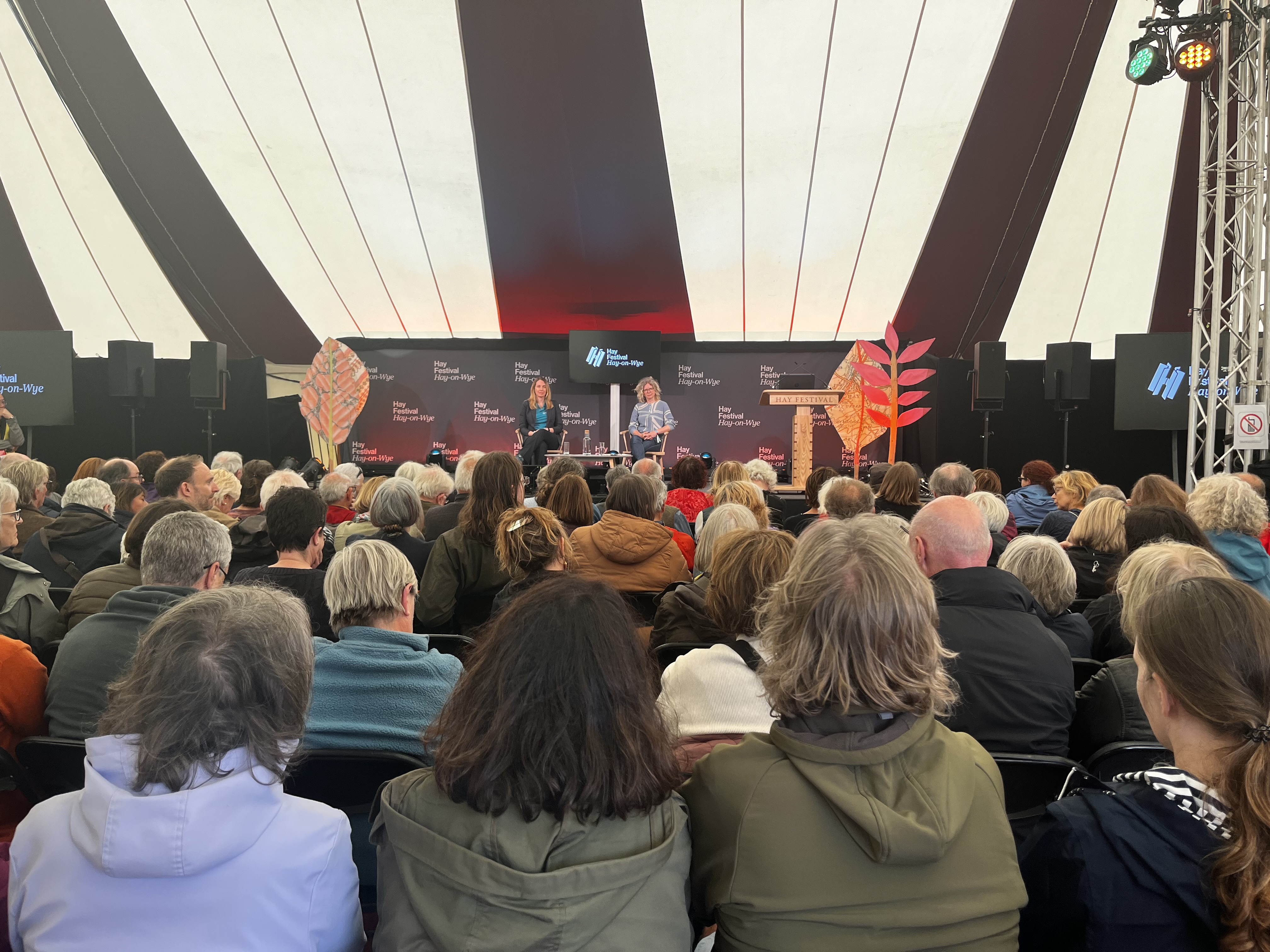 Dr Jennifer Wolowic and Dr Anwen Elias are on stage sitting on chairs, infant of an audience of people at the Hay festival